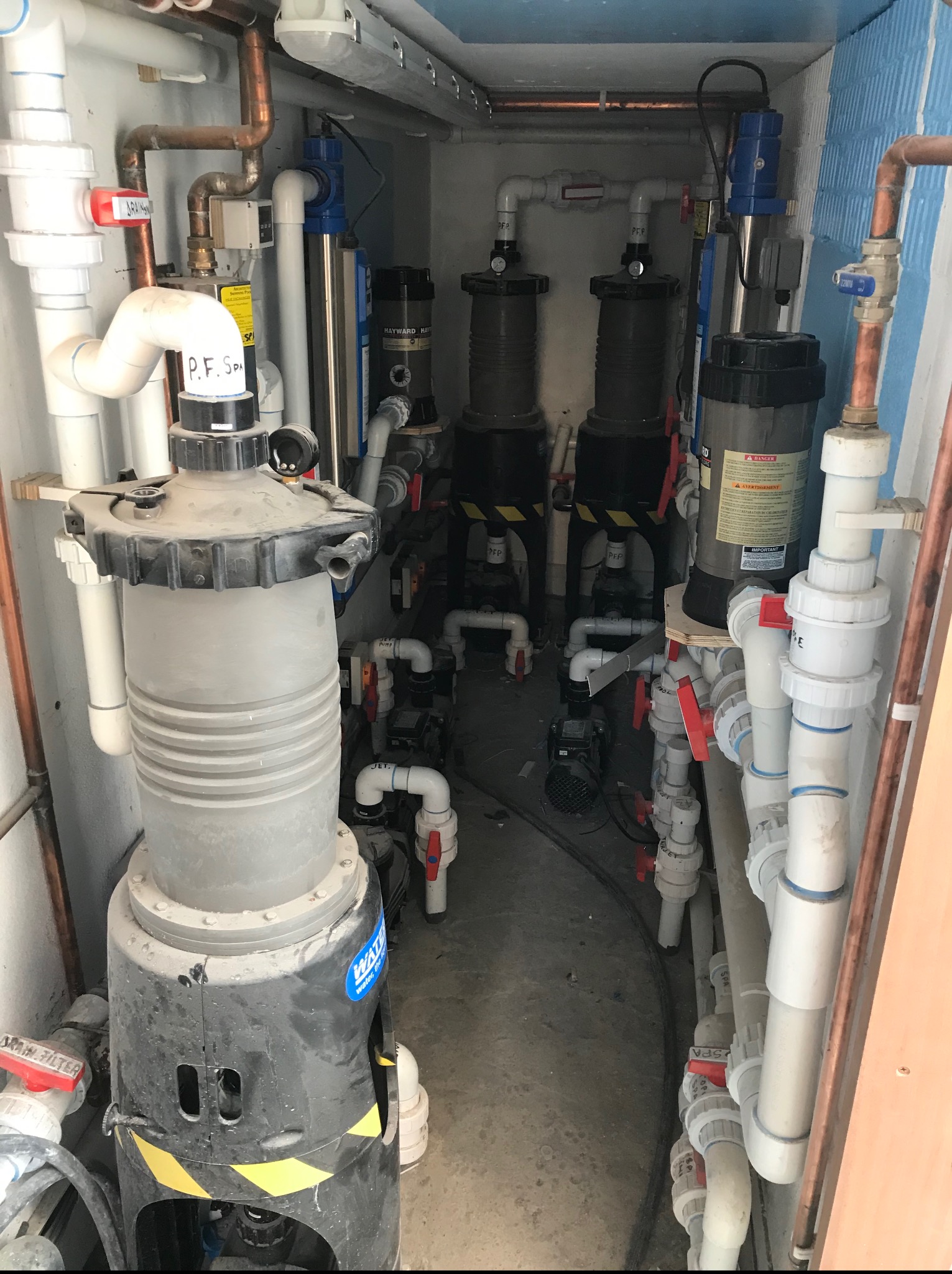 Złożona instalacja hydrauliczna z filtrami i rurami w pomieszczeniu technicznym, prawdopodobnie system filtracji wody basenowej lub spa, widoczne elementy z tworzyw sztucznych i miedzi.