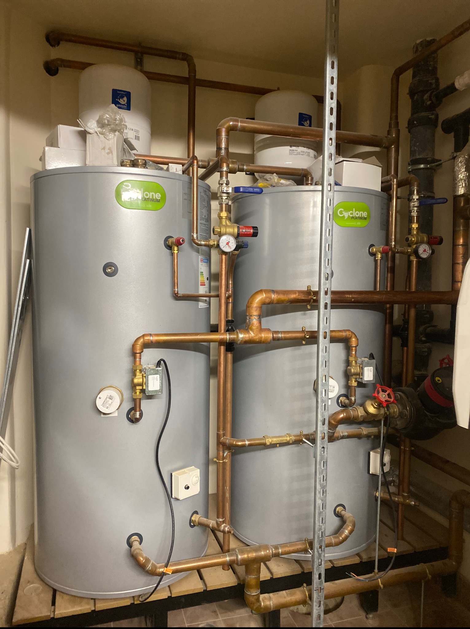 Dwa srebrne bojlery Cyclone Platinum z miedzianą instalacją, zaworami i manometrami w kotłowni. Widoczne rury, złączki i elementy automatyki.