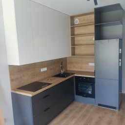 MICHAŁ ZDERSKI EMZZE - Nowoczesna kuchnia z szarymi szafkami dolnymi i białymi górnymi, drewnianym blatem oraz otwartymi półkami z jasnego drewna, oświetlona punktowymi lampami.