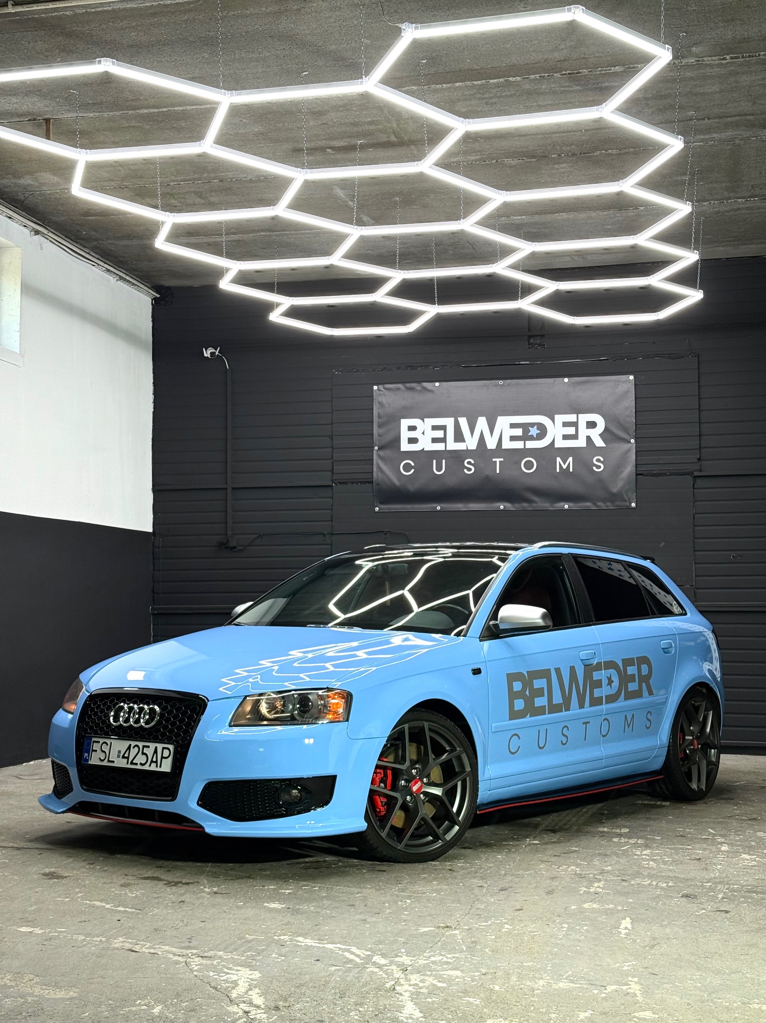 Audi A3 po zmianie koloru folią Hexis na jasnoniebieski, z czarnymi felgami i czerwonymi akcentami, zaparkowany w studiu Belweder Customs.