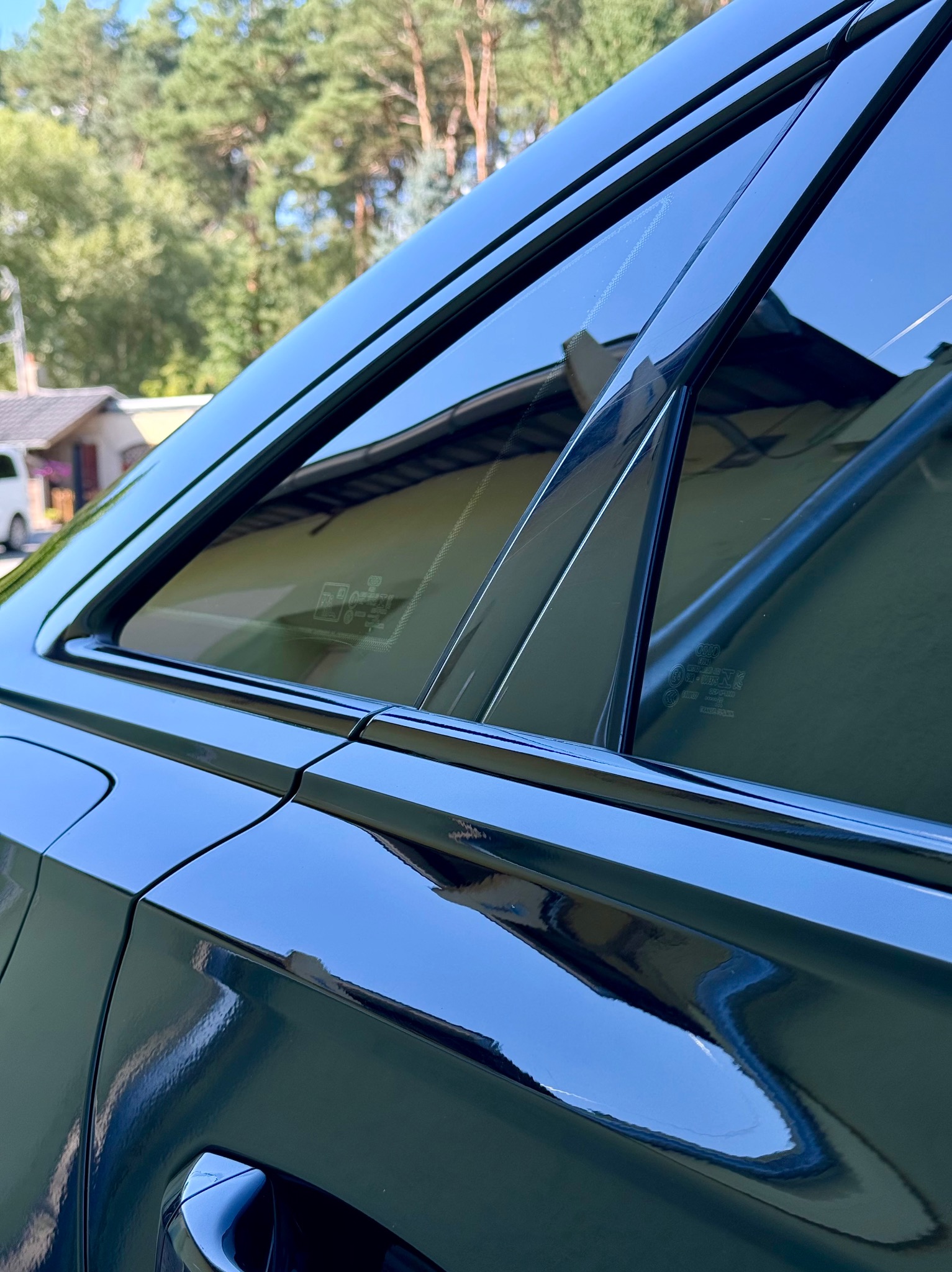 Błyszczący, czarny Audi A6 C8 po dechromingu listw bocznych, z widocznym fragmentem karoserii, szybą i odbijającym się otoczeniem.