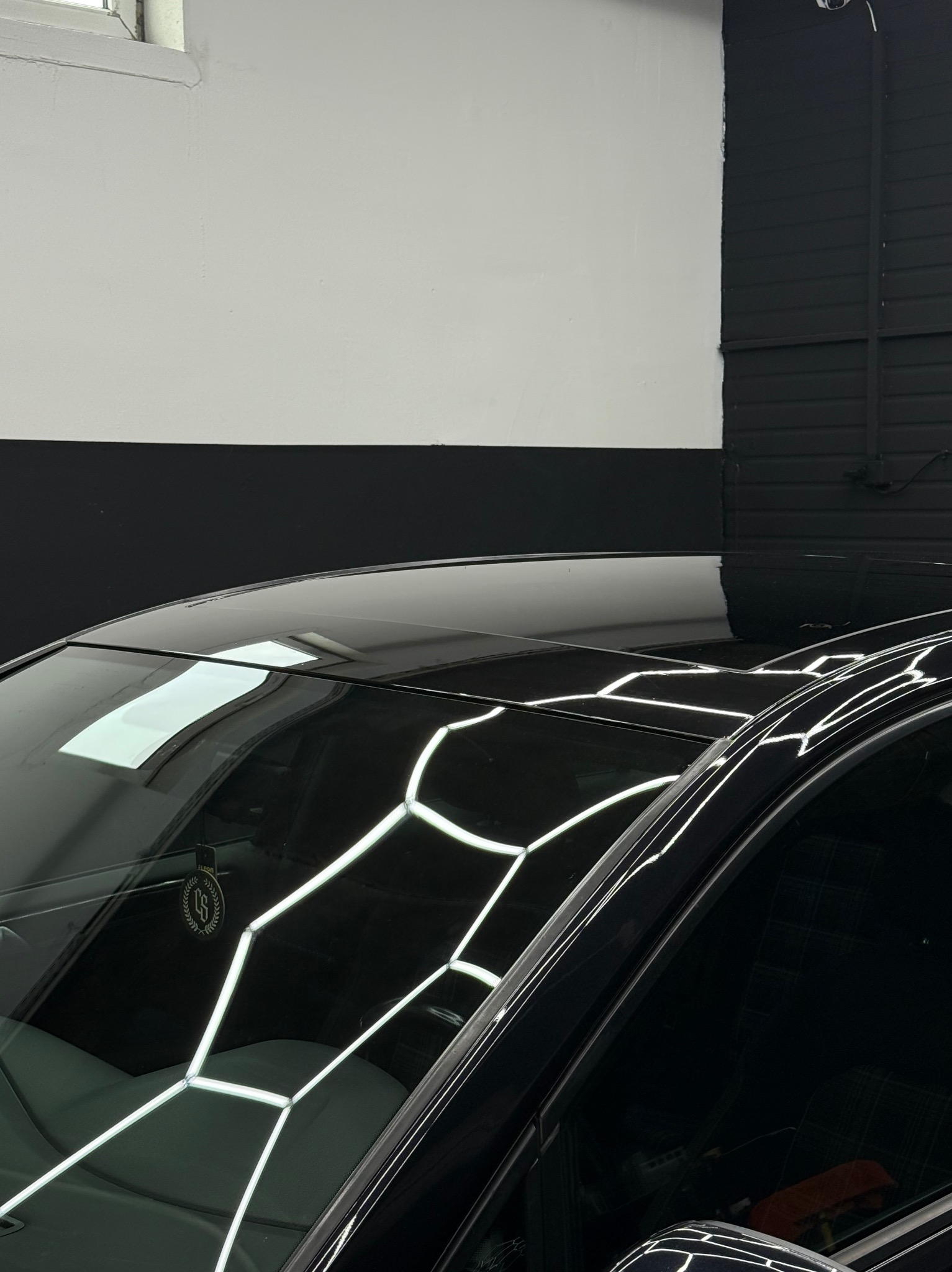 Błyszczący, czarny dach samochodu po detailingu, odbijający światła lamp w studiu. Widoczny fragment wnętrza i zawieszka zapachowa.