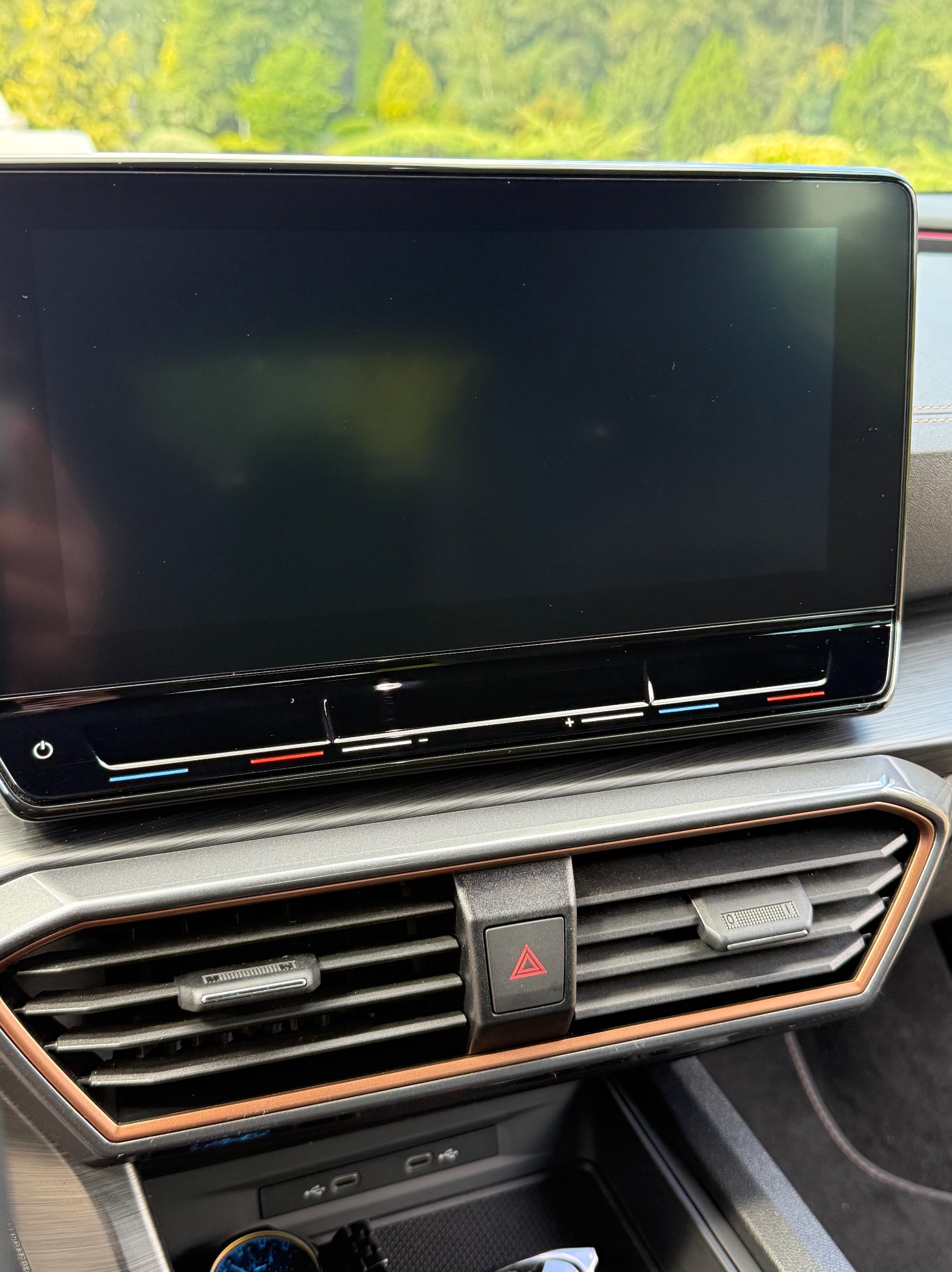 Wnętrze samochodu Cupra z dużym ekranem dotykowym i detalami w kolorze miedzi. Widoczne kratki wentylacyjne i panel sterowania klimatyzacją.