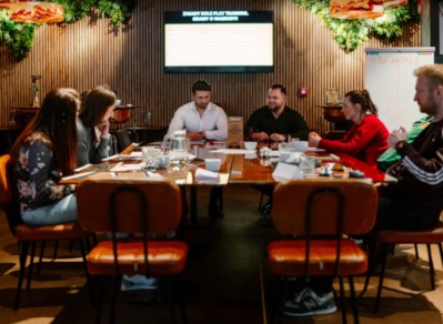 Grupa osób uczestniczy w szkoleniu przy dużym drewnianym stole. Ekran wyświetla tekst 'SMART ROLE PLAY TRAINING'.