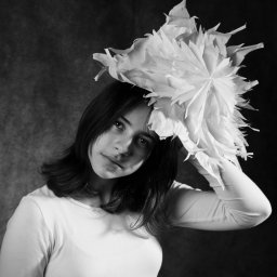 PRO-INVEST - Czarno-biały portret młodej kobiety z dużym, papierowym kwiatem na głowie, spoglądającej w dół, na ciemnym tle.
