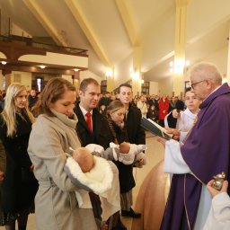 PRO-INVEST - Uroczystość chrztu w kościele: ksiądz w fioletowej szacie błogosławi niemowlęta trzymane przez rodziców, w tle zgromadzeni goście i architektoniczne detale wnętrza.