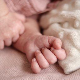 Martyna Kucharska - Drobne dłonie noworodka spoczywają na miękkim, różowym kocyku, delikatnie kontrastując z kremowym futerkiem w tle. Subtelne światło podkreśla detale skóry.