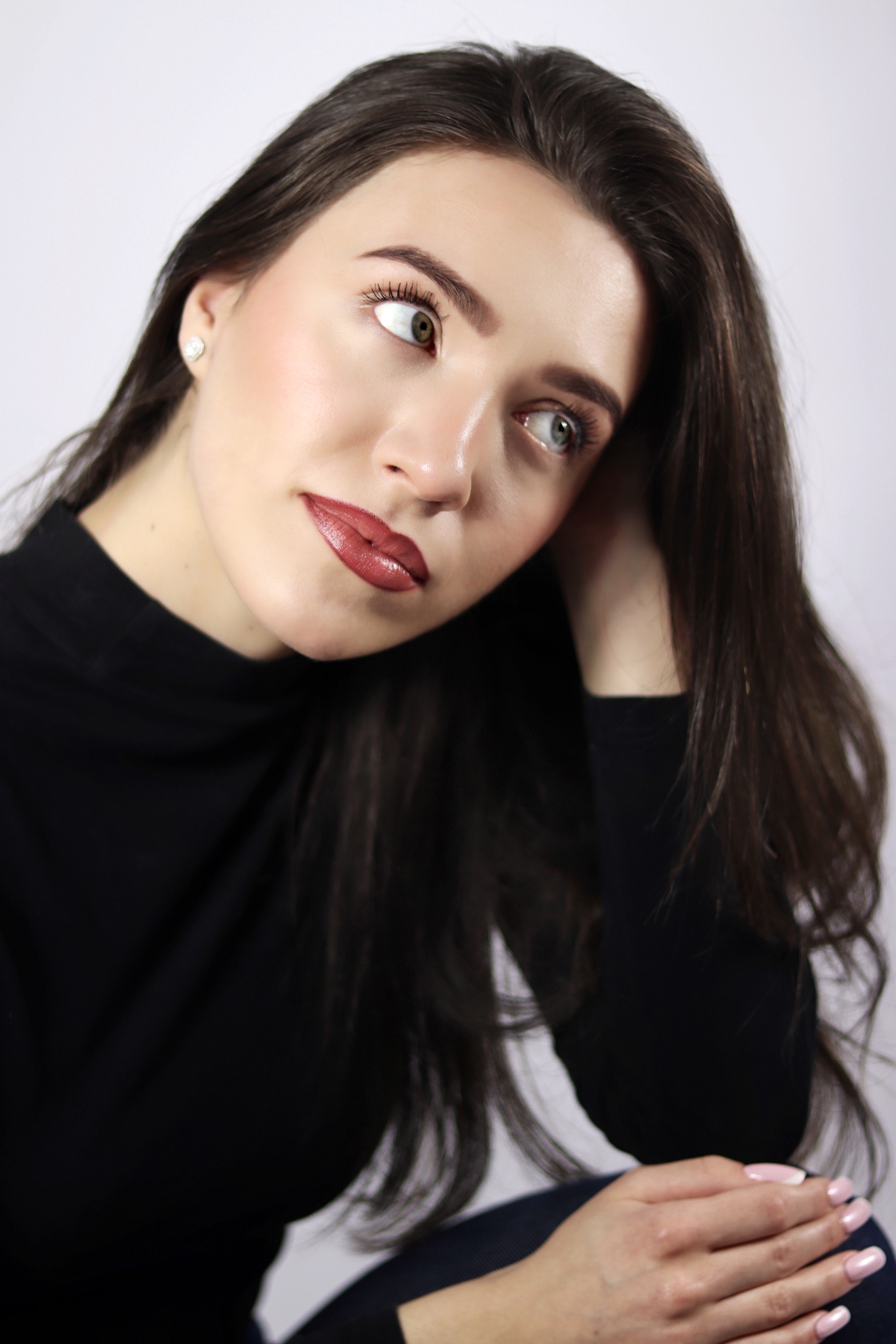 Portret kobiety w czarnym golfie, z długimi, ciemnymi włosami i delikatnym makijażem, spoglądającej w lewo. Subtelne oświetlenie podkreśla rysy twarzy.