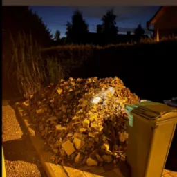 Zdjęcie 'Przed' przedstawia stertę gruzu z cegieł i kamieni obok kosza na śmieci na tle posesji w nocnym oświetleniu. Widoczny fragment chodnika z kostki.