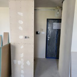 Daniel Dobosz - Montaż ścianki działowej z płyty gipsowo-kartonowej z widocznymi puszkami elektrycznymi i śladami po szpachlowaniu w trakcie prac wykończeniowych.