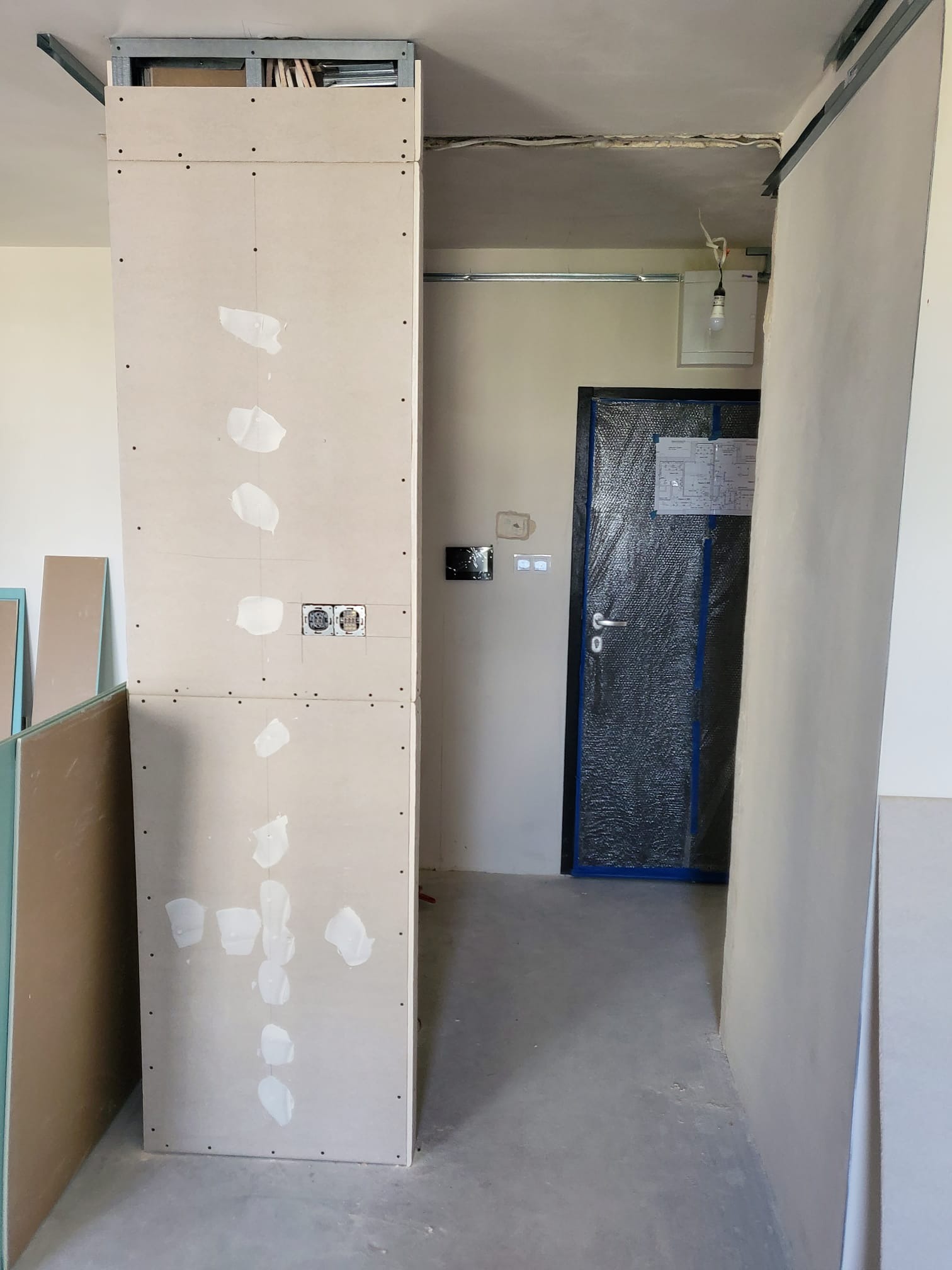 Montaż ścianki działowej z płyty gipsowo-kartonowej z widocznymi puszkami elektrycznymi i śladami po szpachlowaniu w trakcie prac wykończeniowych.