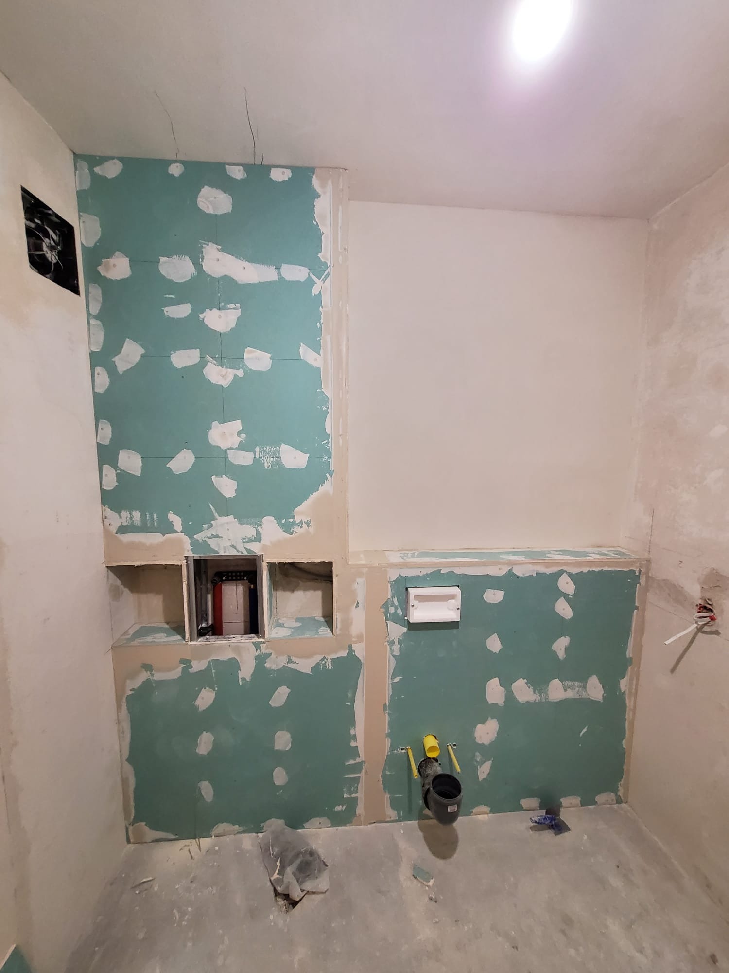 Łazienka w trakcie remontu: ściany z płyt gipsowo-kartonowych, wnęki, instalacja odpływowa. Widoczne ślady szpachlowania i przygotowania do dalszych prac wykończeniowych.