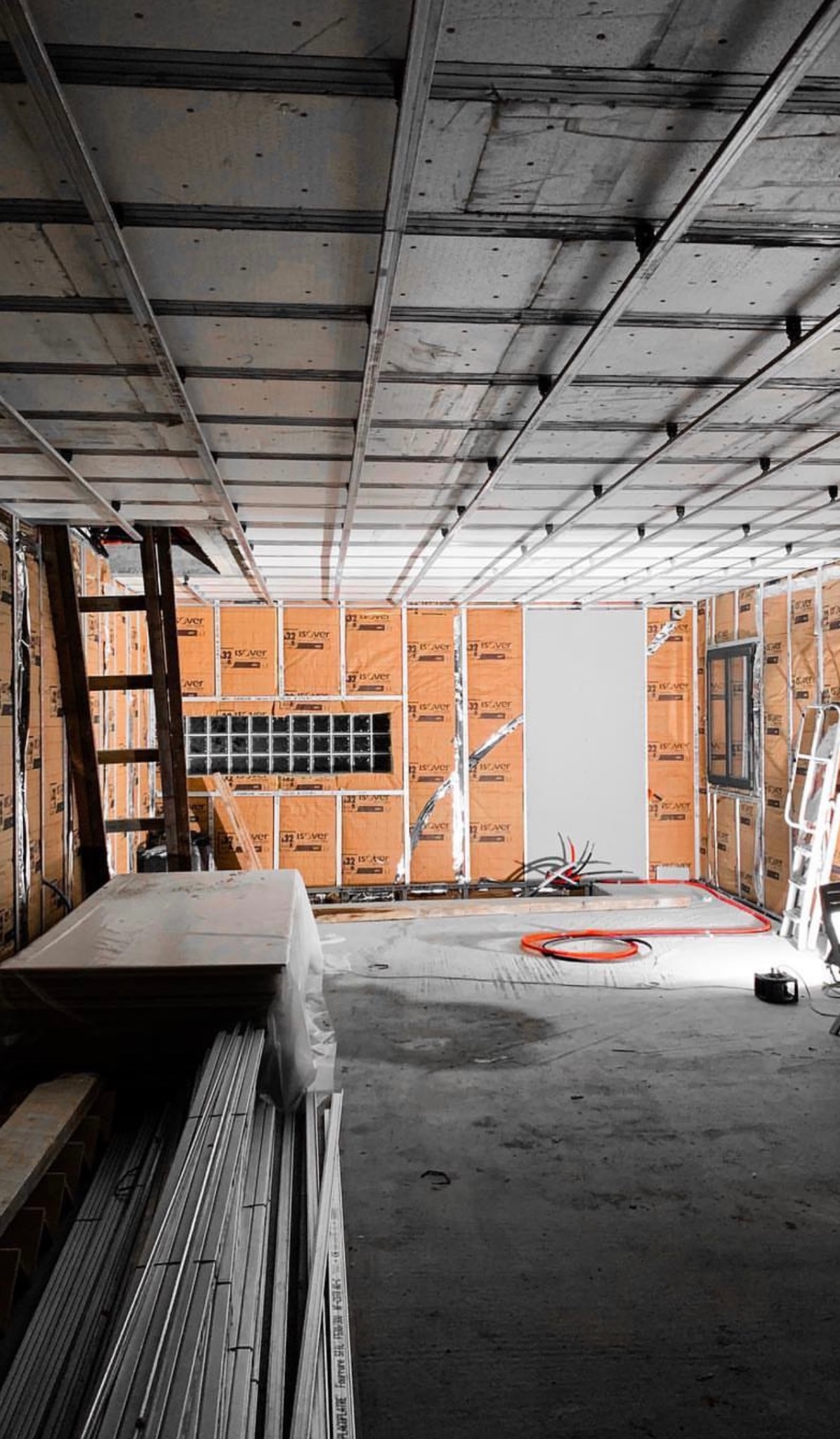 Wnętrze w trakcie prac: montaż stelaża sufitu podwieszanego i izolacji ścian. Widoczne profile, płyty izolacyjne, drabina i instalacje elektryczne.