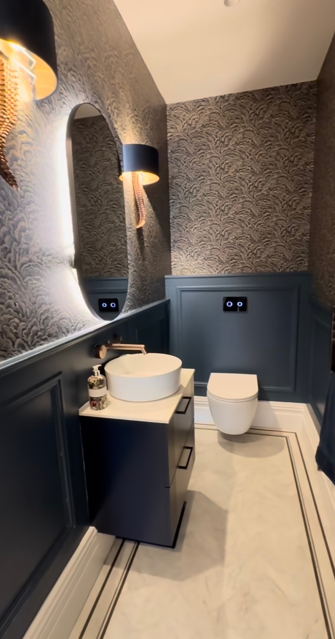 Elegancka łazienka po remoncie: umywalka nablatowa, podświetlane lustro i wzorzysta tapeta. Wykończenie w odcieniach granatu i złota, subtelne oświetlenie.