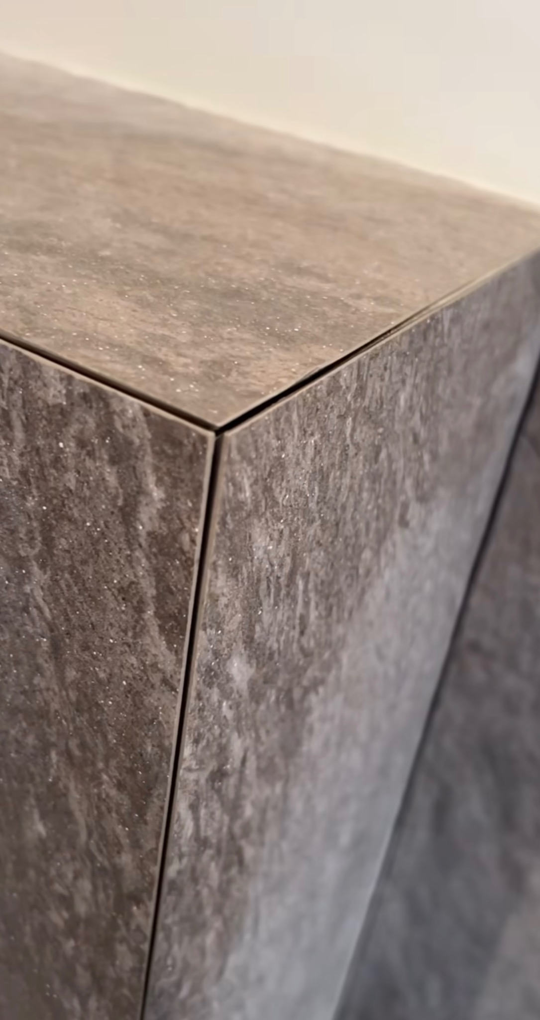 Szczegółowe ujęcie narożnika blatu wykończonego szarymi płytkami imitującymi kamień, z widocznymi fugami i delikatnym połyskiem.