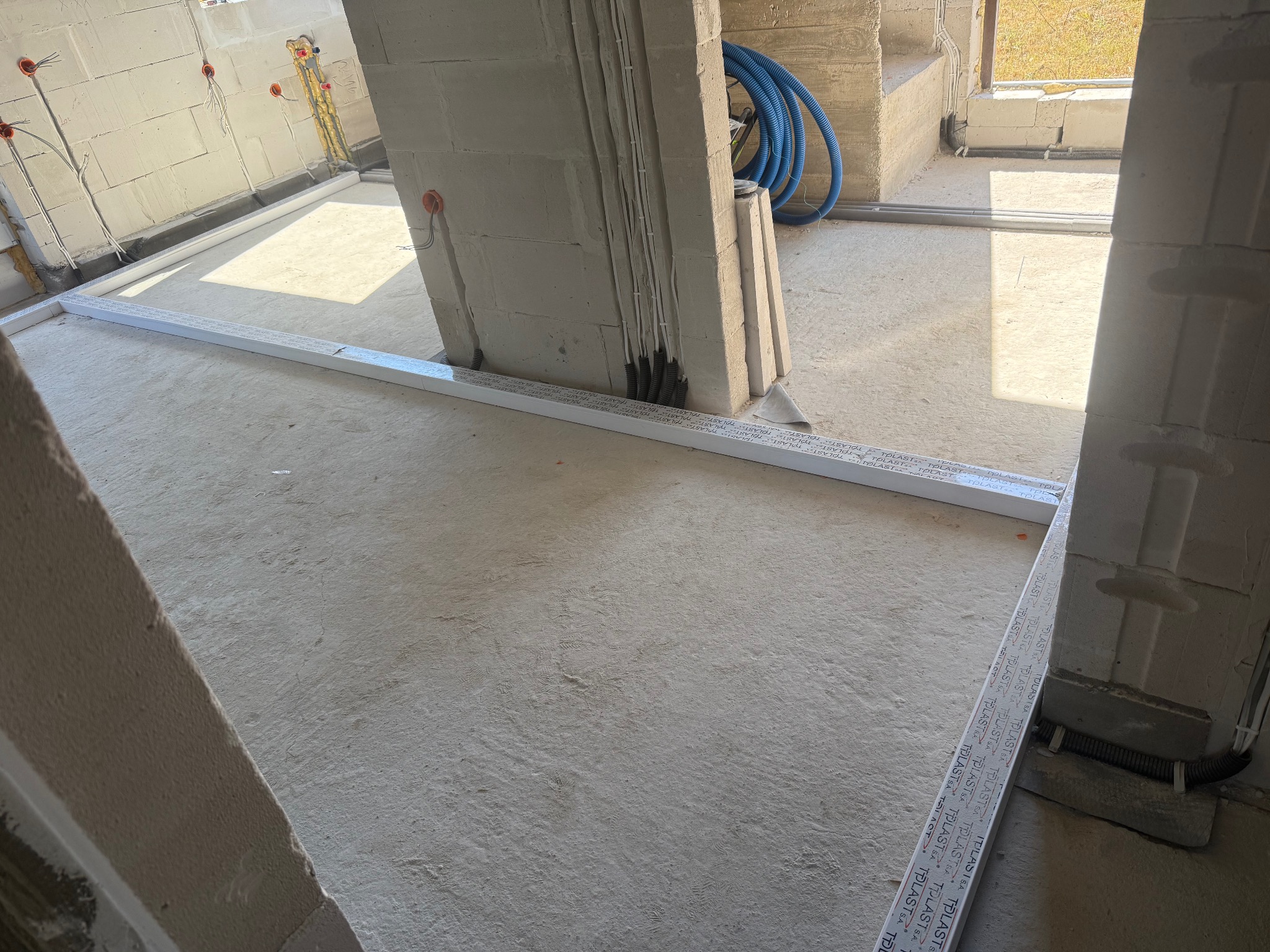 Surowy stan wnętrza w trakcie prac elektrycznych: widoczne kable, puszki instalacyjne w ścianach z betonu komórkowego oraz niebieska rura karbowana w tle.