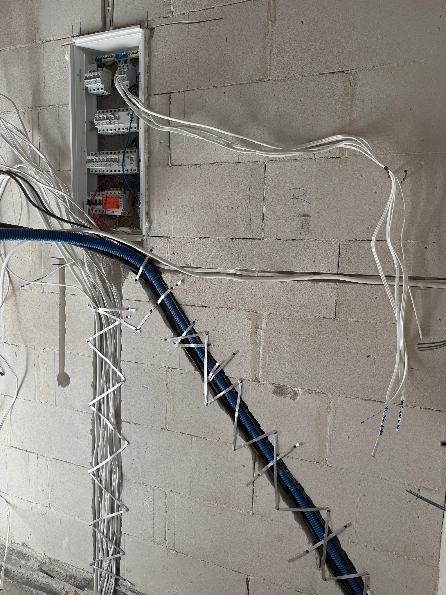 Rozdzielnia elektryczna z przewodami ułożonymi w bruzdach ściany z betonu komórkowego, zabezpieczone metalowymi uchwytami. Instalacja w trakcie montażu.