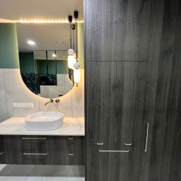 ClearSpace - Nowoczesna łazienka z okrągłym lustrem podświetlanym LED, umywalką nablatową i ciemnymi szafkami z drewnopodobnym wykończeniem. Minimalistyczny design.