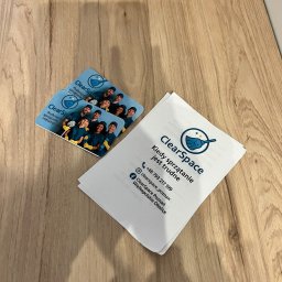 ClearSpace - Wizytówki i ulotka ClearSpace na drewnianym blacie. Wizytówki prezentują zespół, ulotka hasło: Kiedy sprzątanie jest trudne. Kontakt i logo firmy sprzątającej.