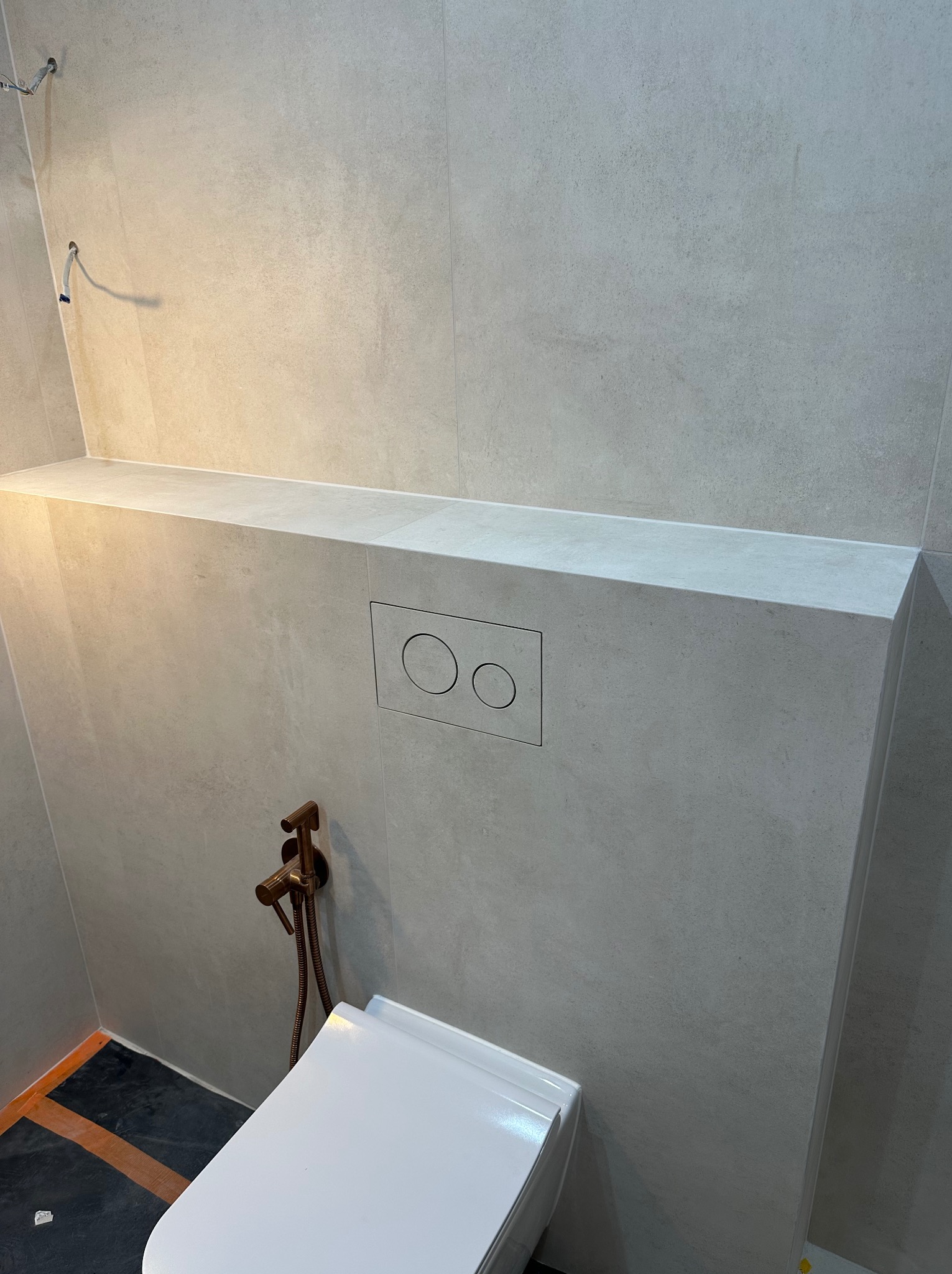 Wykończona łazienka z podtynkową spłuczką WC i bidetką w kolorze miedzi. Płytki w odcieniach szarości, minimalistyczny design.