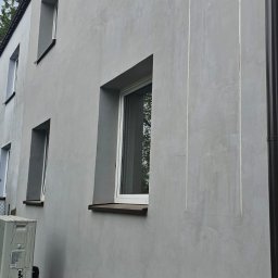 EKOENERGIA I AUTOMATYKA SPÓŁKA Z OGRANICZONĄ ODPOWIEDZIALNOŚCIĄ - Szara elewacja budynku po renowacji z widocznymi pionowymi liniami, okna w szarych ramach, rura spustowa i klimatyzator na tle zieleni.