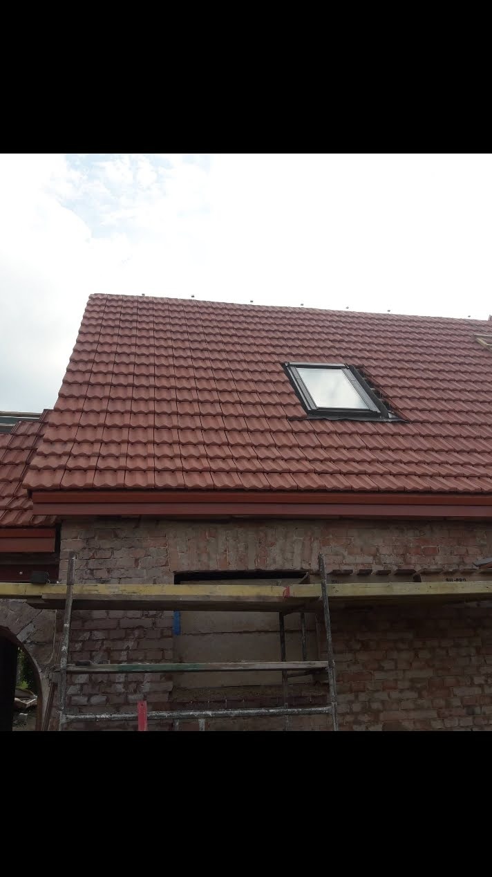Czerwony dach z dachówką ceramiczną i oknem dachowym, widok z rusztowania. Nowe krycie dachu na tle ceglanej ściany.