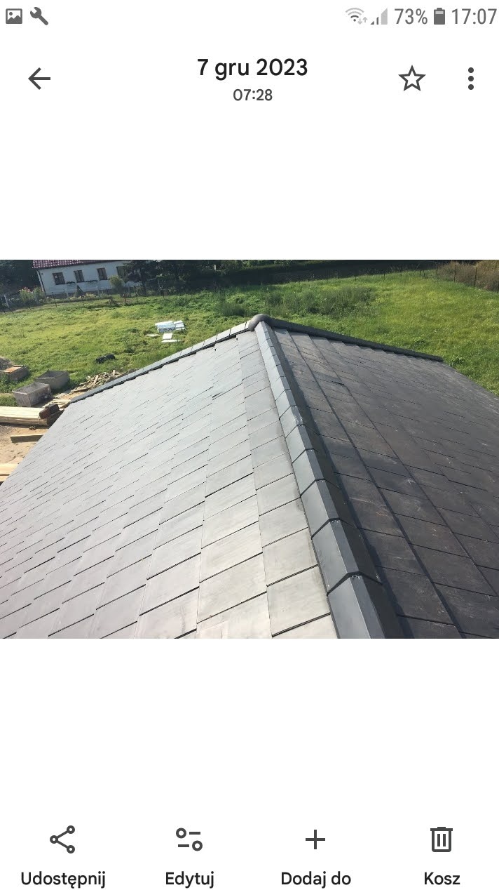 Ukończony dach z szarej dachówki karpiówki, widok z góry, w tle zielona trawa i dom. Precyzyjne ułożenie, estetyczne wykończenie.