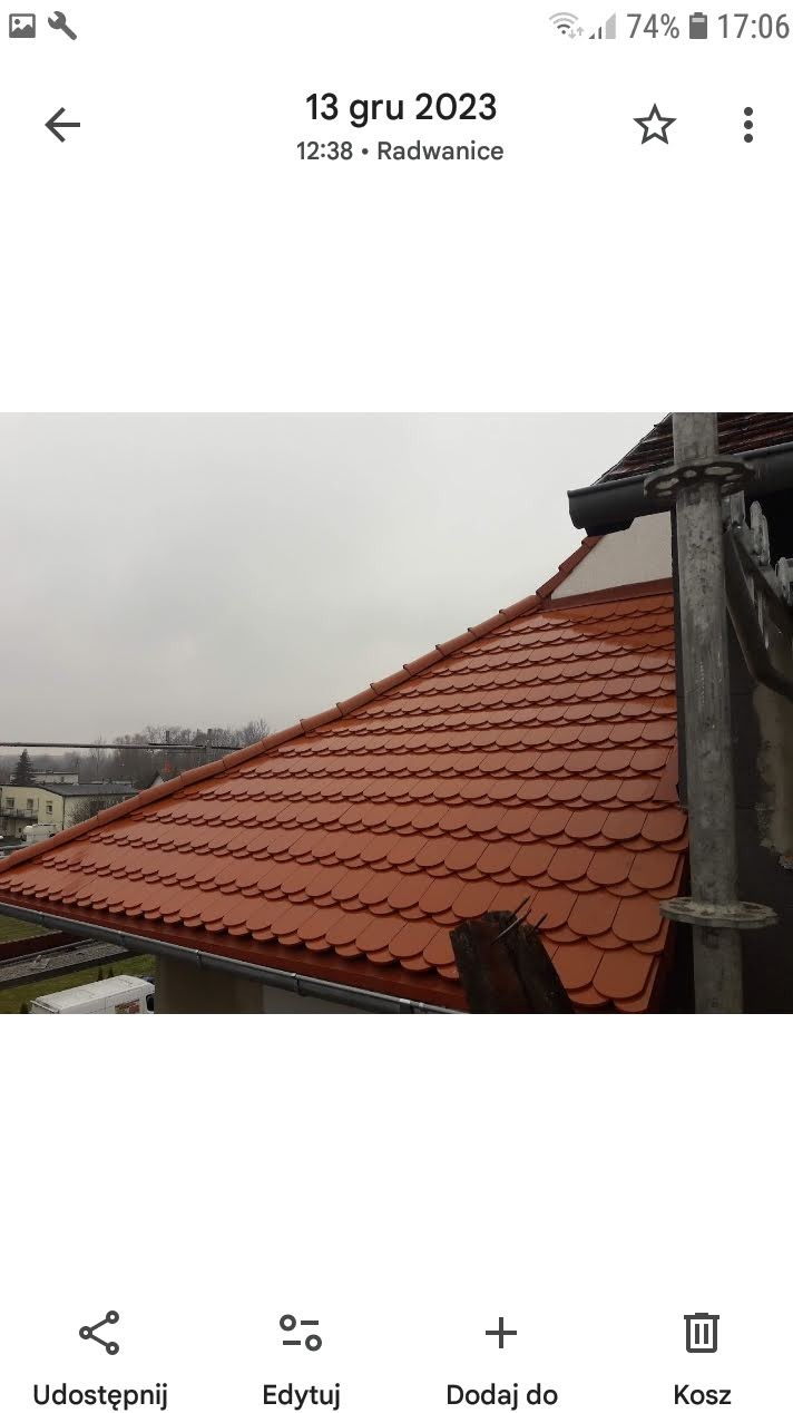 Nowy dach z dachówki ceramicznej w odcieniach czerwieni, widoczny z boku, z elementami rusztowania po prawej stronie. Pochmurne niebo w tle.