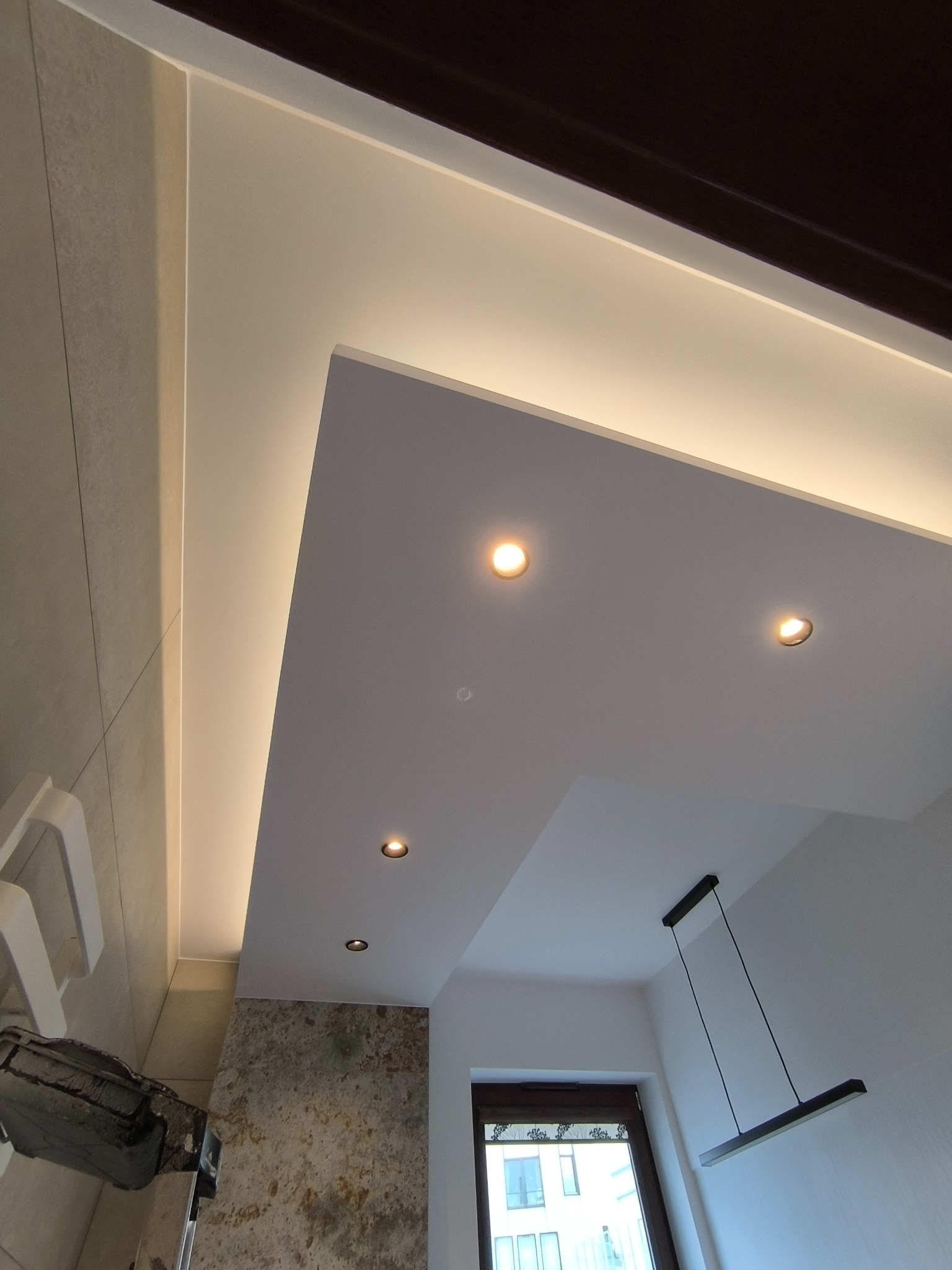 Oświetlenie sufitowe LED w łazience: punktowe i taśmowe, z widocznymi fragmentami ściany z płytek i elementami wyposażenia.