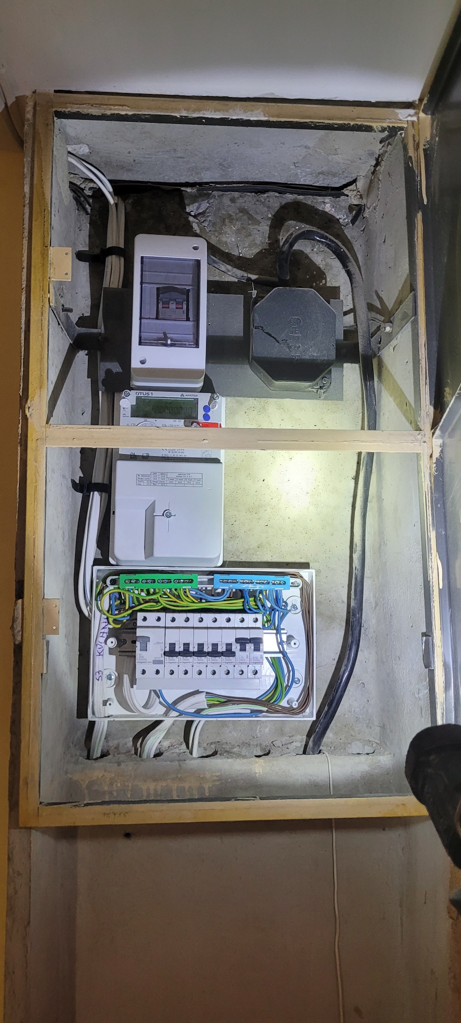 Zamknięta skrzynka elektryczna z licznikiem i bezpiecznikami, widok z bliska, oświetlenie górne, kable w listwach.