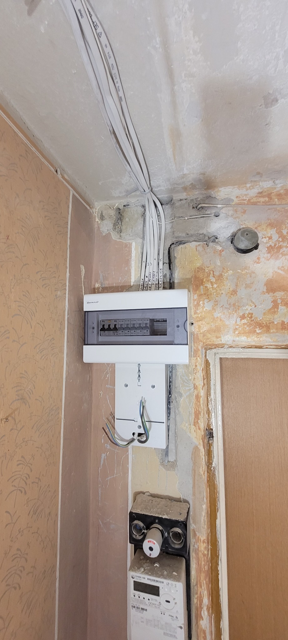 Nowa skrzynka elektryczna z bezpiecznikami zamontowana na ścianie w trakcie remontu, z widocznymi przewodami i starym licznikiem.