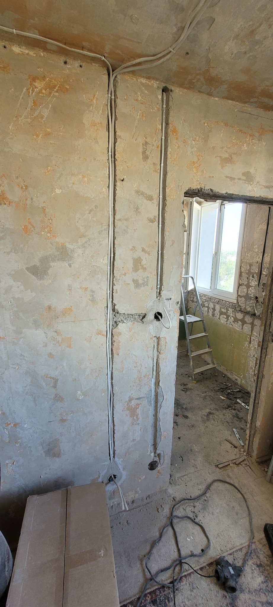 Bruzdy pod instalację elektryczną w ścianie z widocznymi kablami i puszkami, surowy stan ścian przed malowaniem, drabina w tle, remont instalacji.