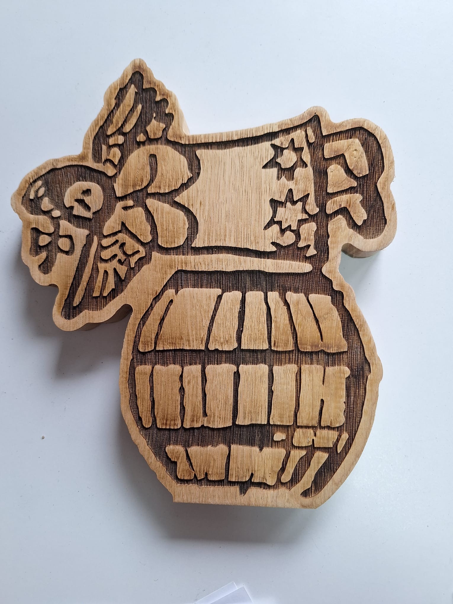 Drewniana płaskorzeźba przedstawiająca stylizowaną beczkę z wygrawerowanymi elementami roślinnymi i gwiazdami, wykonana techniką CNC na jasnym tle.