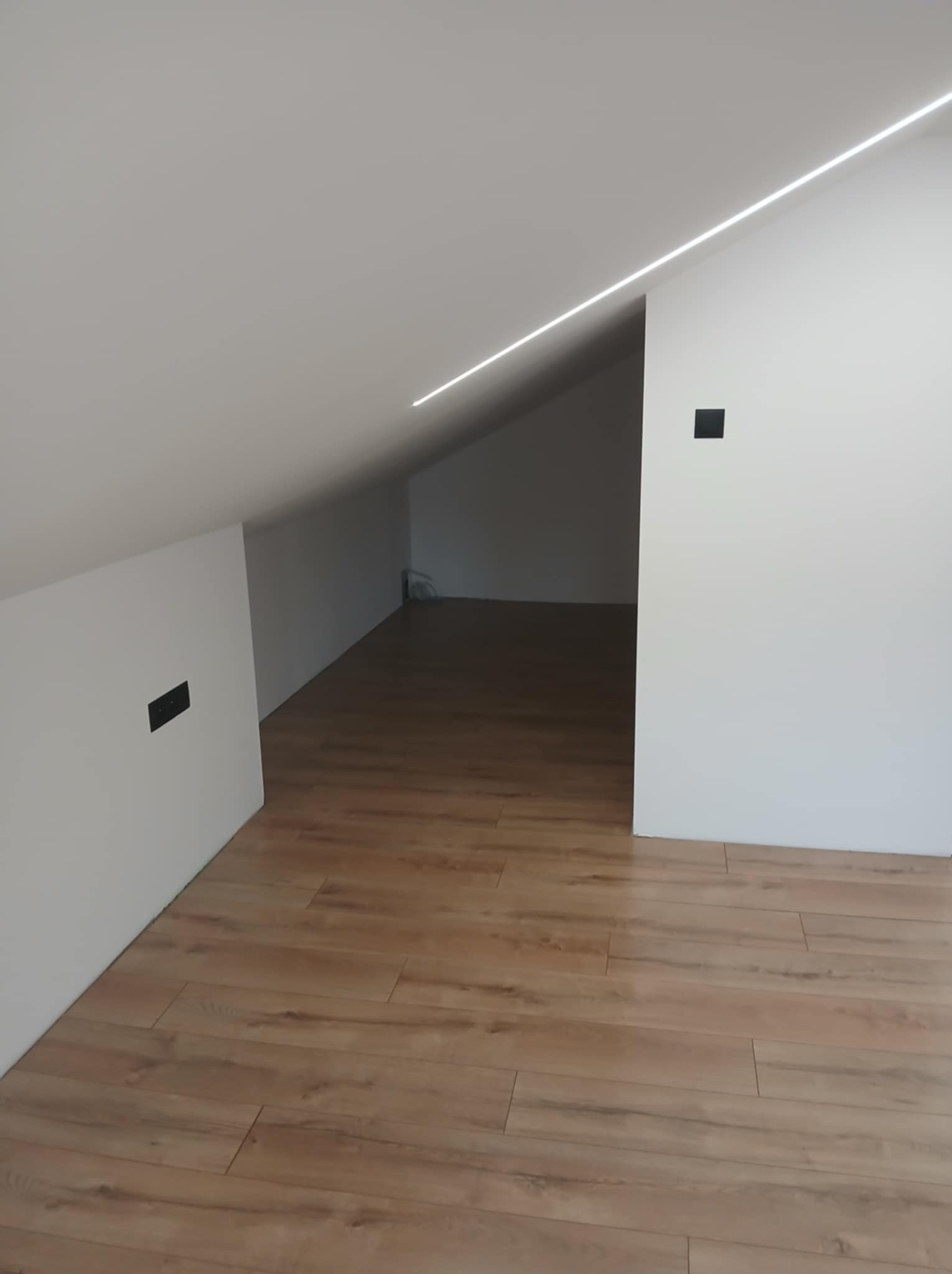 Nowoczesne oświetlenie LED w skosach poddasza, z czarnymi gniazdkami. Jasne panele podłogowe. Minimalistyczny design.