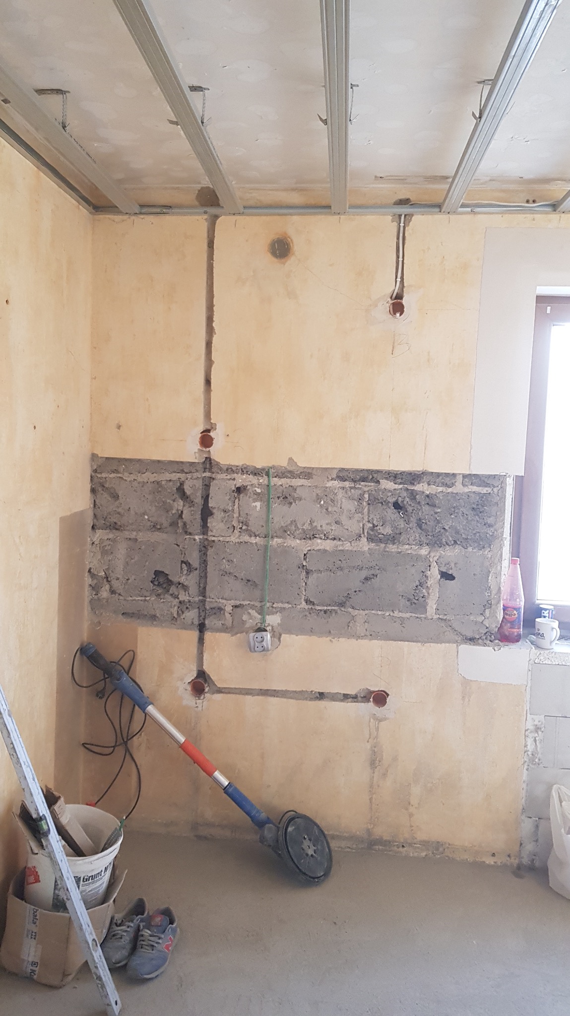 Wnętrze w trakcie remontu: wyfrezowane bruzdy pod instalację elektryczną w ścianie, widoczne puszki i przewody. Na podłodze narzędzia i materiały budowlane.