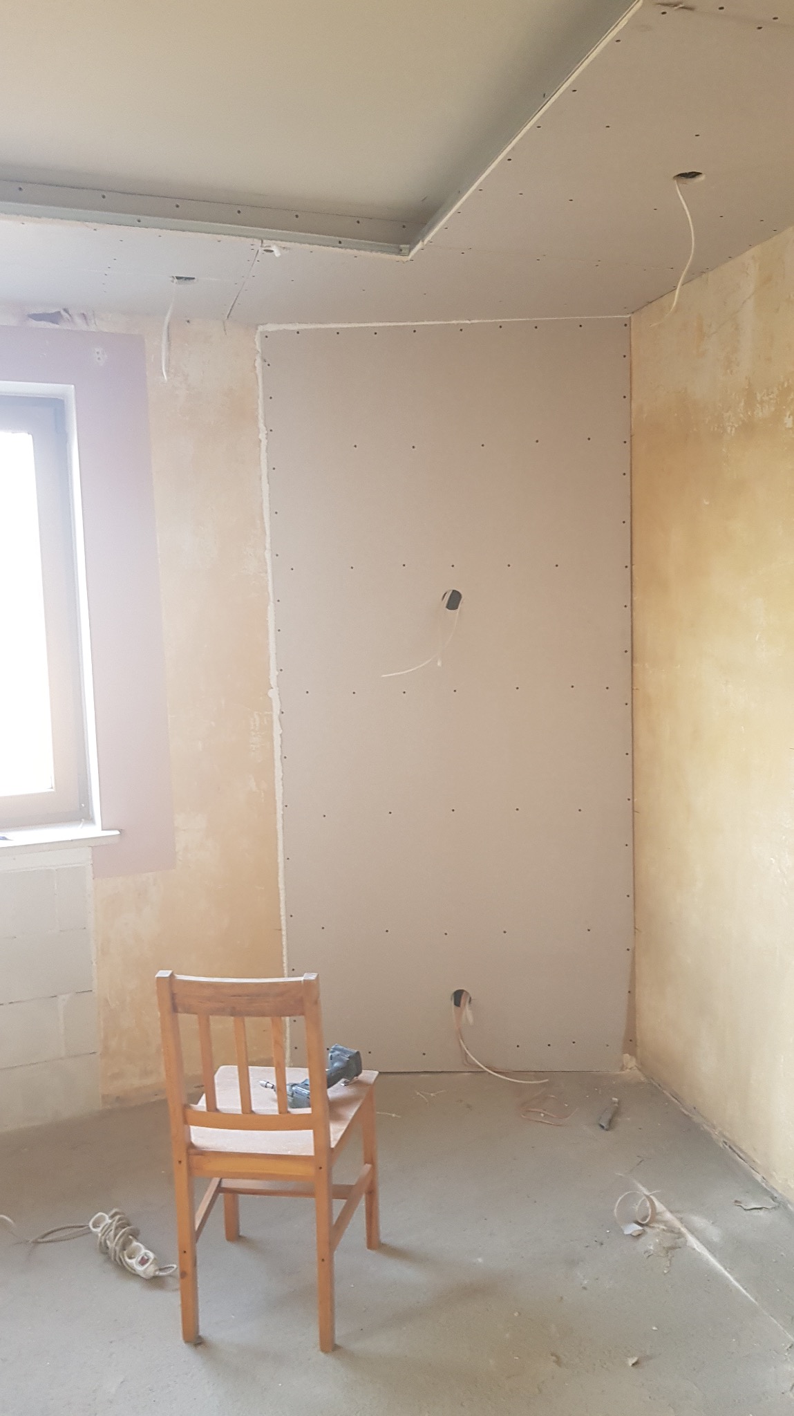 Wnętrze w trakcie montażu płyt gipsowo-kartonowych na ścianie i suficie. Widoczne przewody elektryczne, krzesło i narzędzia.