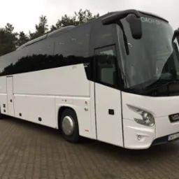 Nowoczesny, biały autokar VDL z czarnymi szybami i napisem 'COACH OF THE YEAR' nad przednią szybą, zaparkowany na tle drzew.