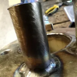 Spoina spawalnicza łącząca rurę z metalową podstawą. Widoczne ślady obróbki na rurze i charakterystyczne zabarwienia po spawaniu.