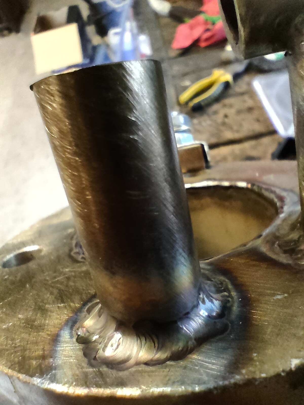 Spoina spawalnicza łącząca rurę z metalową podstawą. Widoczne ślady obróbki na rurze i charakterystyczne zabarwienia po spawaniu.