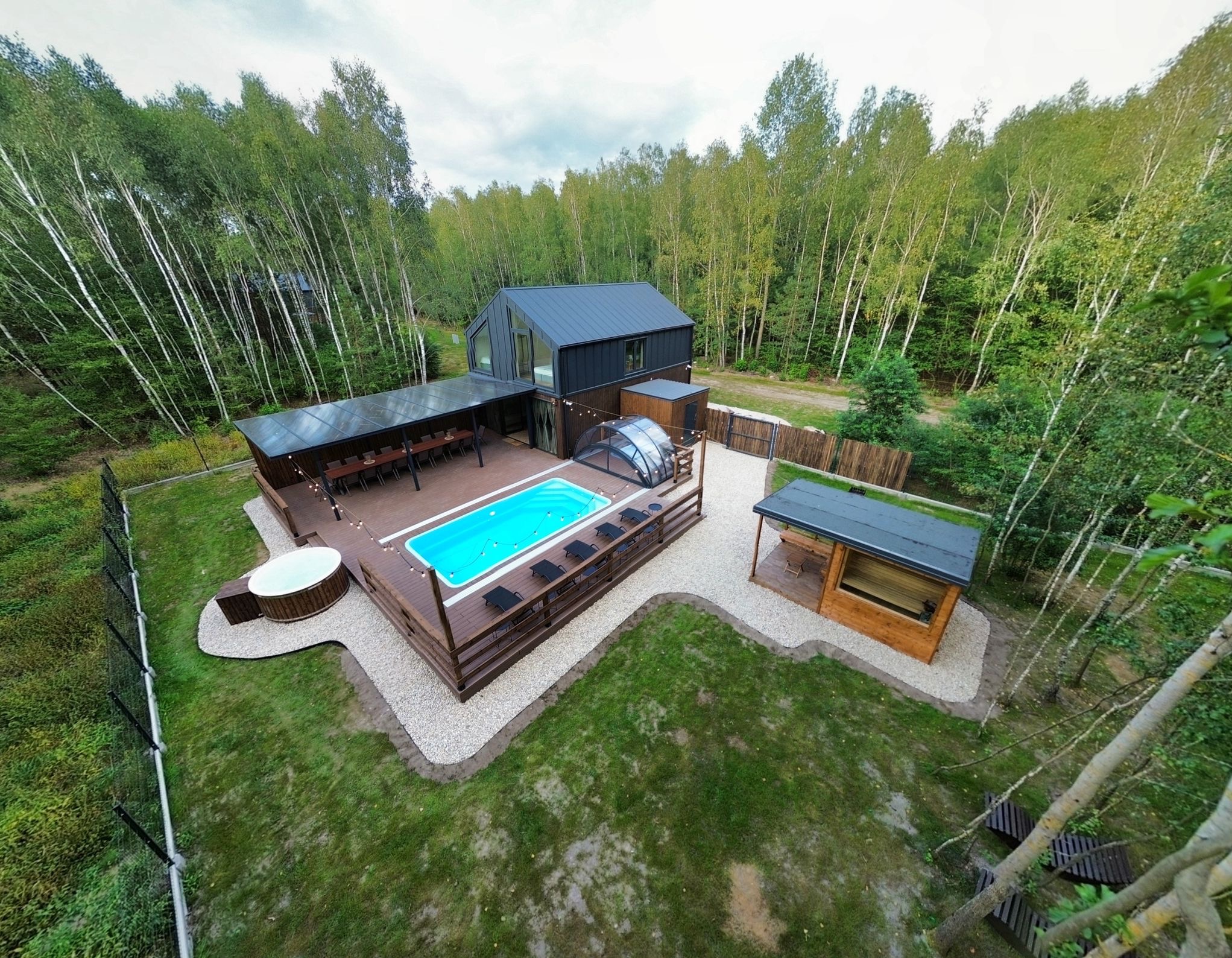 Nowoczesny dom z tarasem, basenem i jacuzzi w leśnym otoczeniu. Drewniana zabudowa, oświetlenie girlandami, elegancki design.