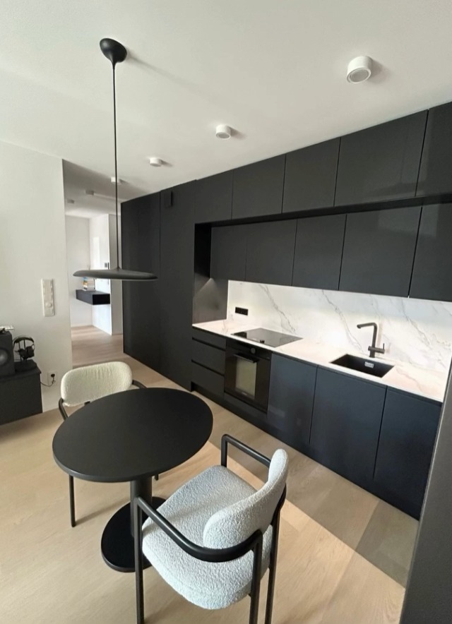 Nowoczesna, czarna zabudowa kuchenna z marmurowym blatem i okrągłym stołem w Krakowie. Minimalistyczny design, oświetlenie punktowe i wisząca lampa.