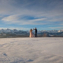 Julita Chudko Photography - Para w strojach ślubnych na tle ośnieżonych Tatr, w promieniach zachodzącego słońca. Delikatna suknia panny młodej i ciemny garnitur pana młodego kontrastują z bielą śniegu.