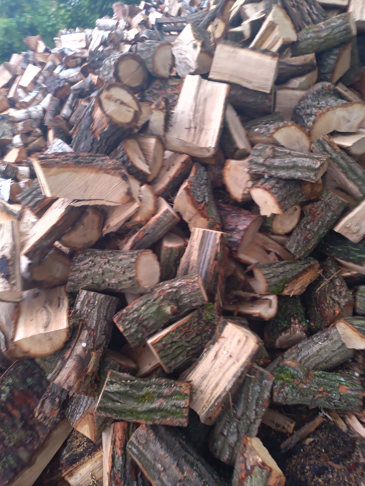 Stos pociętego drewna kominkowego z widoczną korą i jasnym drewnem wewnątrz, ułożonego w nieuporządkowany sposób na zewnątrz.
