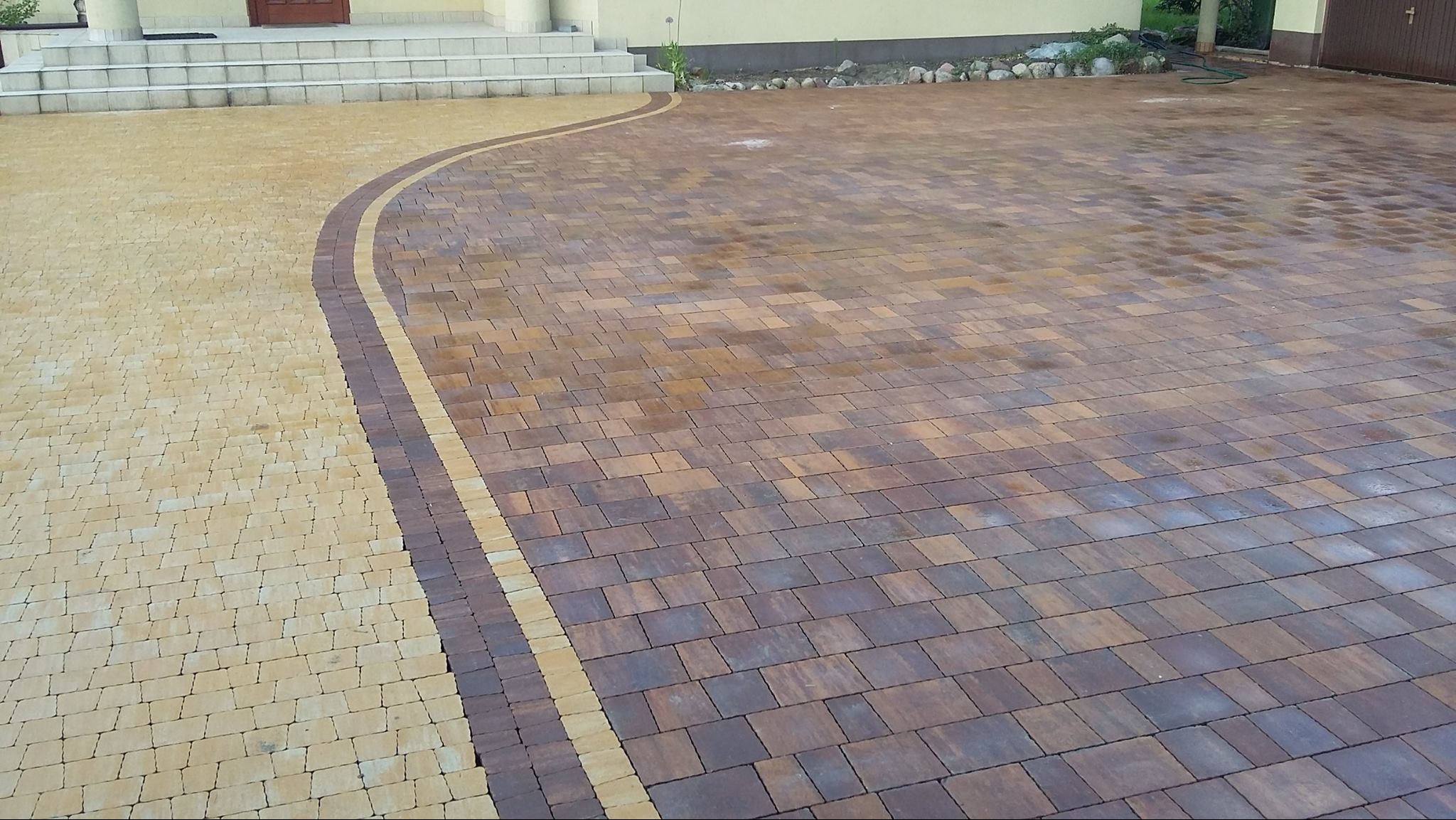 Dwukolorowa kostka brukowa ułożona wzorem łuku przy schodach wejściowych. Ciemnobrązowa kostka na podjeździe, jasna przy schodach. Widok z góry.