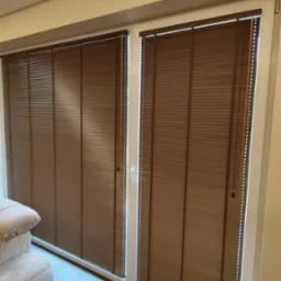 Brązowe plisy okienne zamontowane na dwuskrzydłowym oknie balkonowym z białymi ramami, widok z wnętrza pomieszczenia.