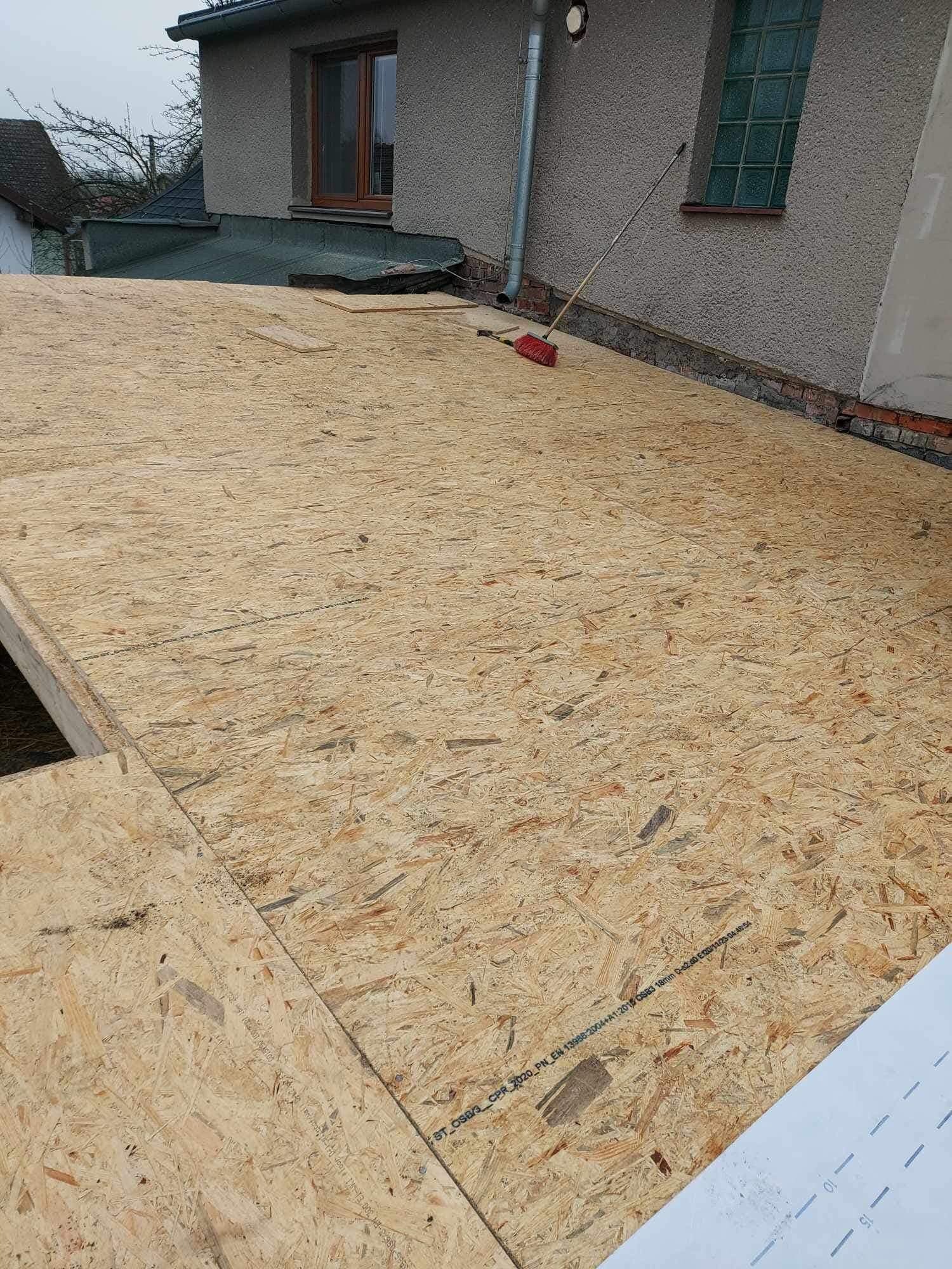 Dach w trakcie budowy: płyty OSB ułożone na konstrukcji, widoczna ściana budynku z oknem, rynna i miotła. Etap prac dekarskich, przygotowanie do krycia.