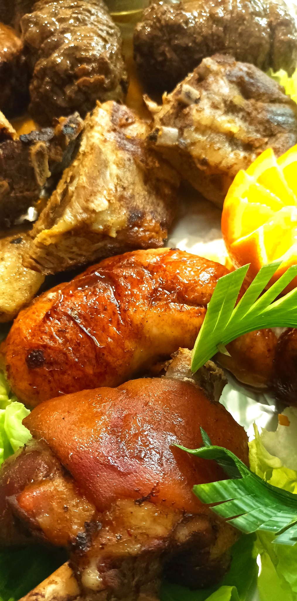 Bogato zdobiony półmisek z pieczonymi mięsami, żeberkami i golonką, udekorowany zielenią i pomarańczą, prezentowany z bliska.