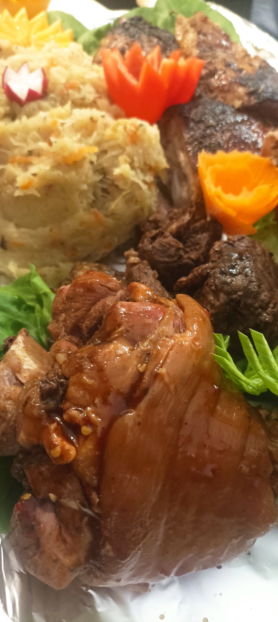 Udekorowany półmisek z golonką, kaszą i pieczenią, ozdobiony pomarańczą i rzodkiewką. Bliski kadr, widoczne detale potraw. Idealne na catering świąteczny.