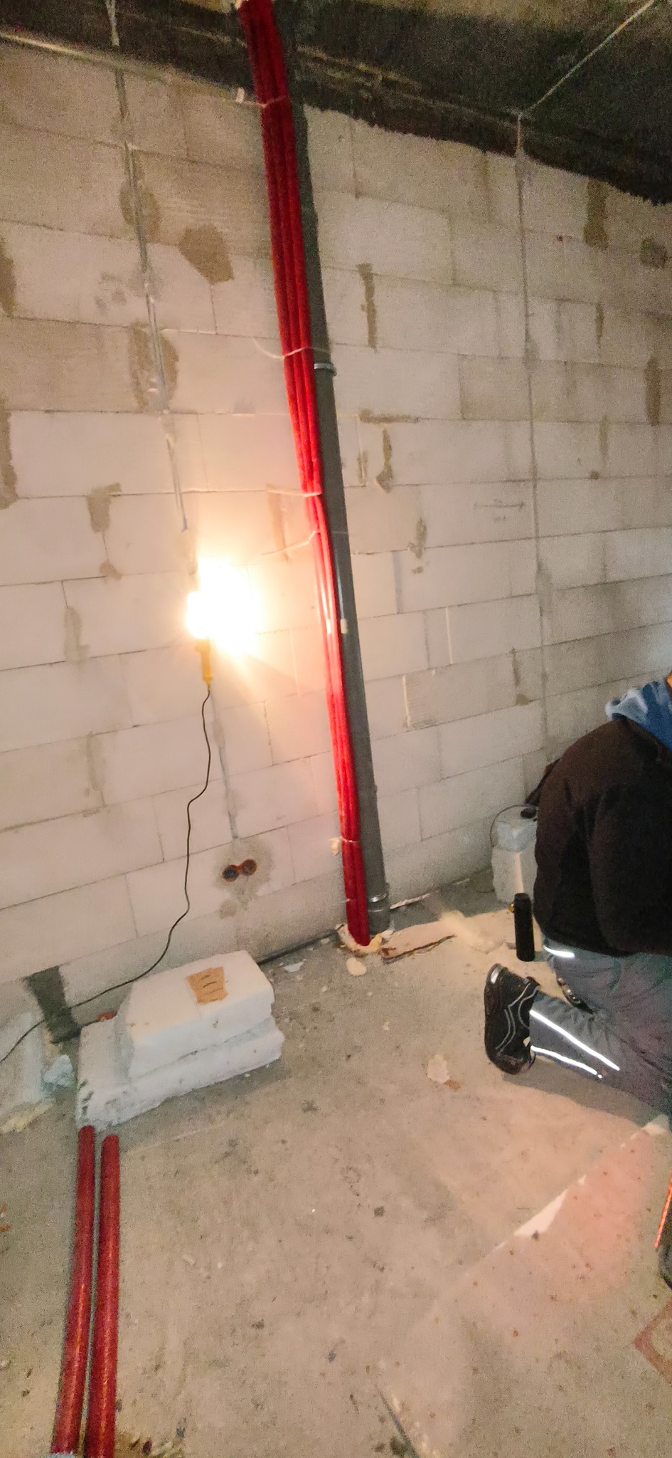 Czerwone rury instalacji grzewczej przy ścianie z betonu komórkowego, oświetlone lampą budowlaną w Jaworznie. Widoczny fragment instalatora podczas pracy.
