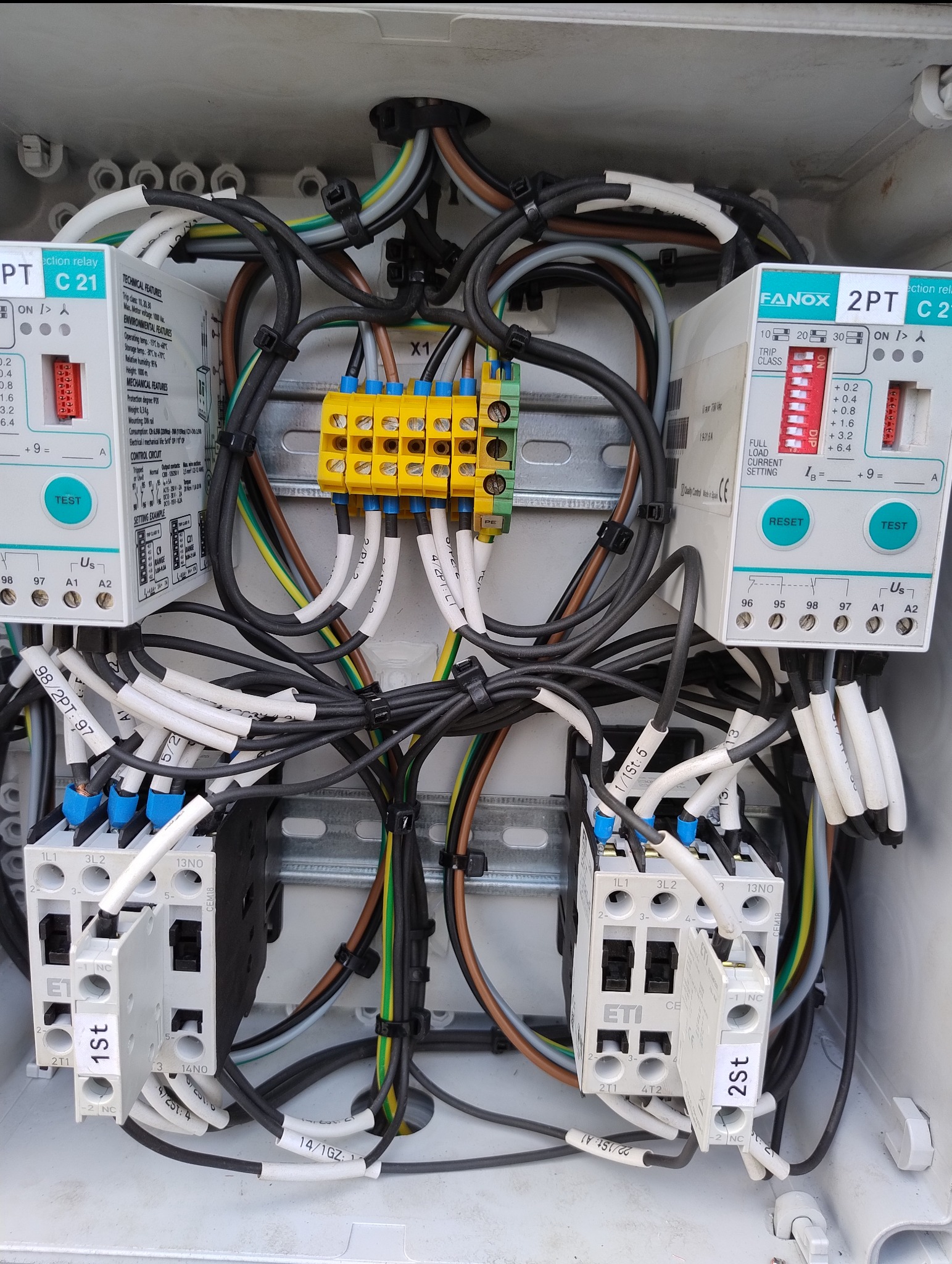 Rozdzielnica elektryczna z zainstalowanymi zabezpieczeniami, przewodami oznaczonymi etykietami i złączkami, wewnątrz plastikowej obudowy. Widok z bliska.